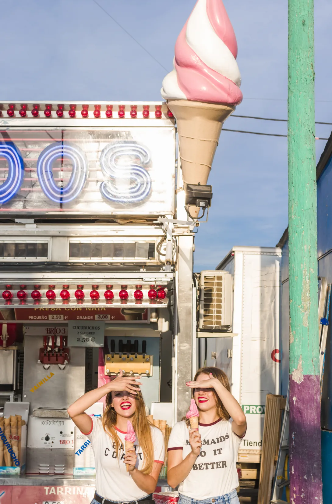 Lágyfagylaltot értékesítő üzlet előtt 2 vidám, fiatal lány lágyfagylalttal a kezében